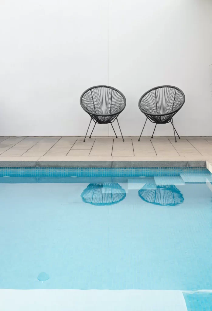Dos sillas junto a una piscina, frente a una pared blanca