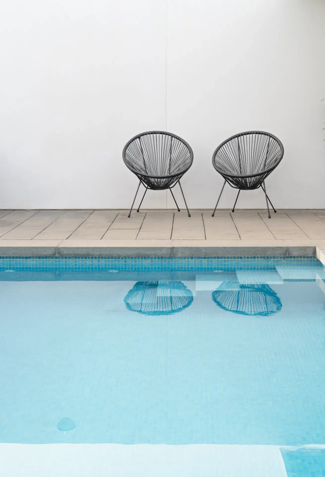 Dos sillas junto a una piscina, frente a una pared blanca