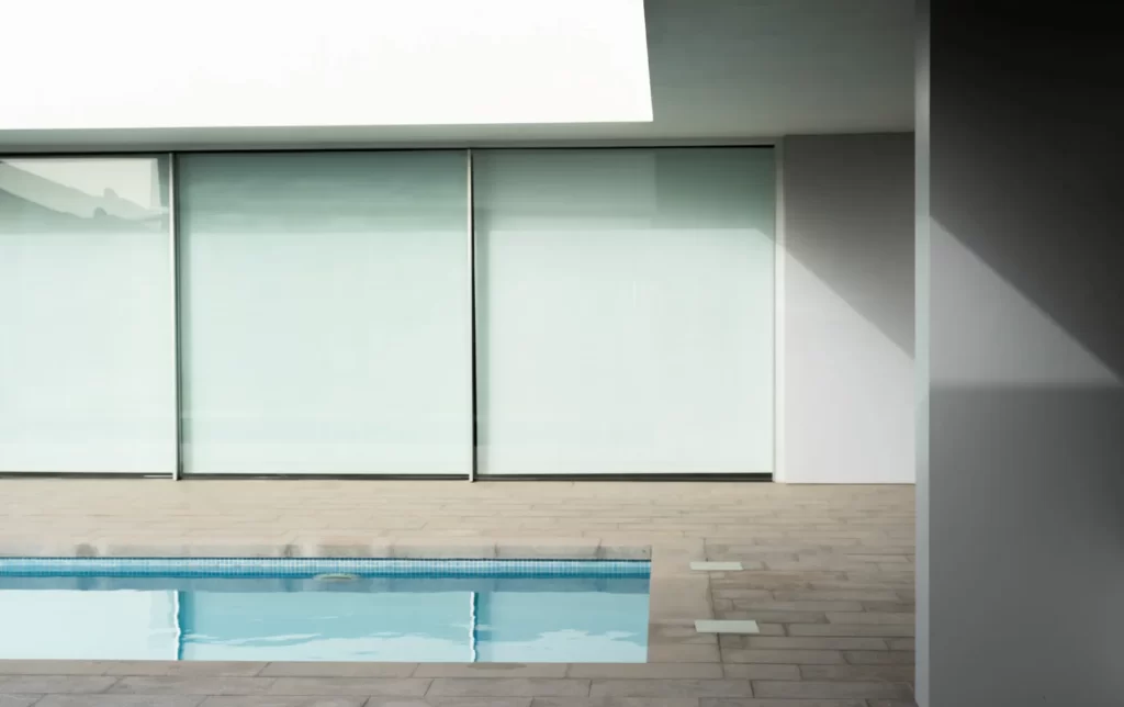 Piscina frente a una fachada de cristal en una vivienda de líneas blancas