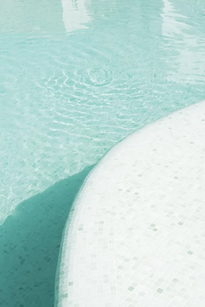 Agua turquesa de una piscina sobre un escalón curvo revestido de gresite blanco y verde