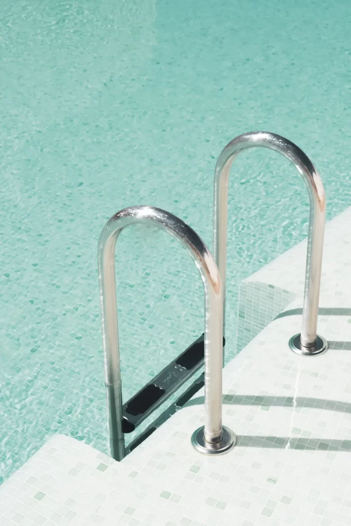 Escalera metálica de una piscina con gresite verde agua y agua transparente