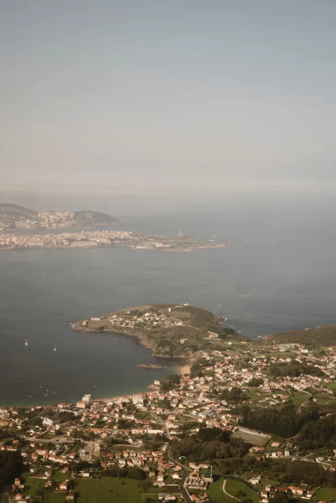 Vista aérea de la costa con un pueblo en primer plano, la bahía y la ciudad al fondo entre bruma