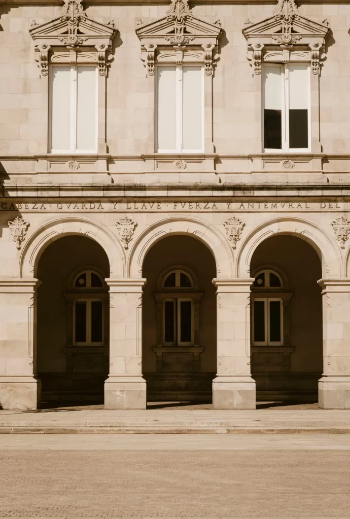Fachada de piedra con tres arcos de medio punto, ventanas con frontones ornamentados y una inscripción en el friso