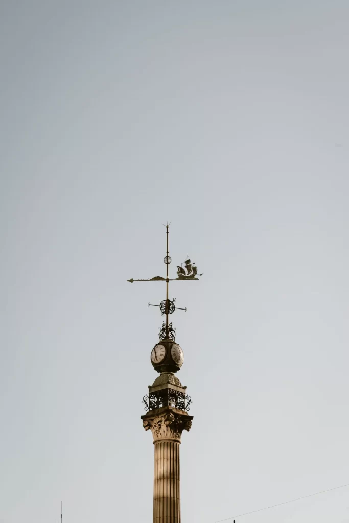 Columna de piedra coronada por un reloj de dos esferas y una veleta con forma de velero