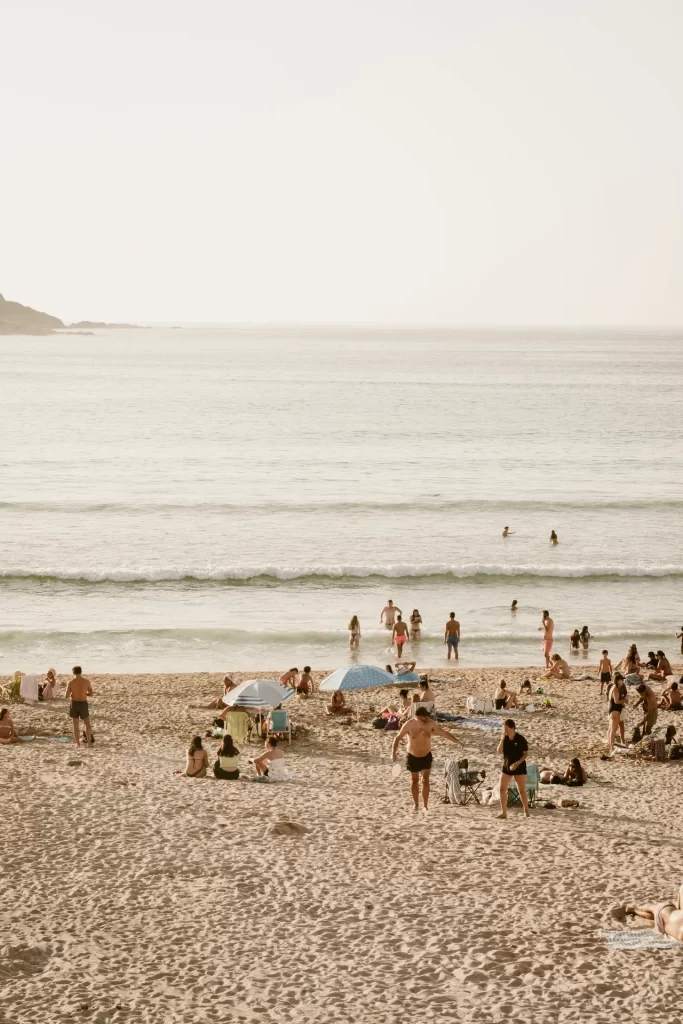 Playa de arena con bañistas, sombrillas y gente entrando al mar bajo la luz cálida de la tarde