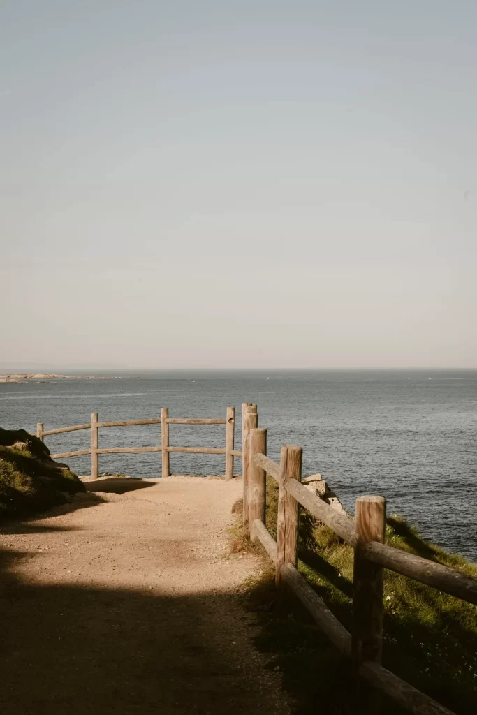 Camino de tierra junto al mar bordeado por una valla de troncos de madera sobre el acantilado