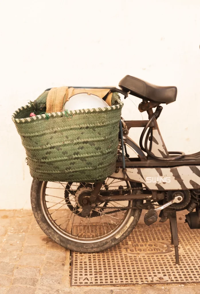 Ciclomotor aparcado junto a una pared blanca con una cesta de palma verde