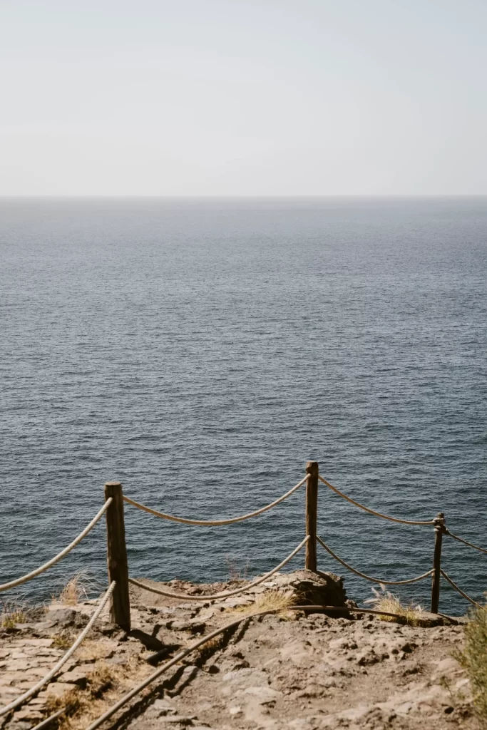 Barandilla de postes de madera y cuerda al borde de un acantilado frente al mar