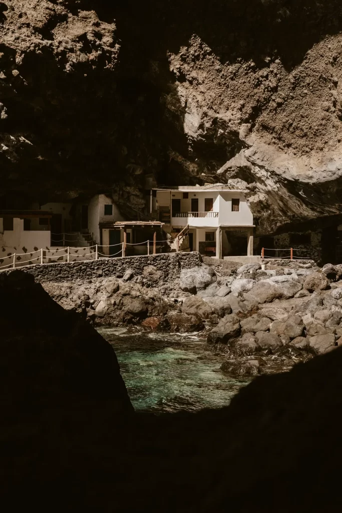 Casas blancas bajo una gran roca junto a una cala de agua turquesa