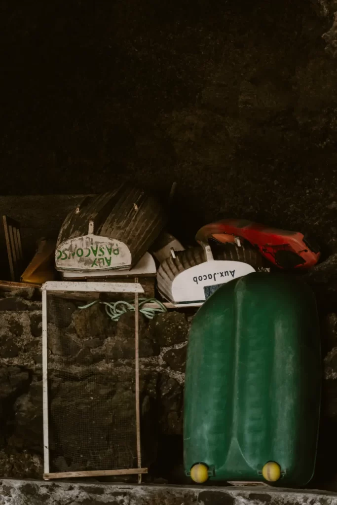 Botes pequeños volcados y un kayak rojo guardados en una cueva con muro de piedra volcánica