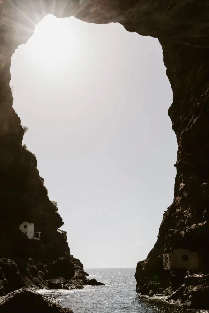 Boca de una cueva marina a contraluz que enmarca el mar y pequeñas casas blancas en la roca