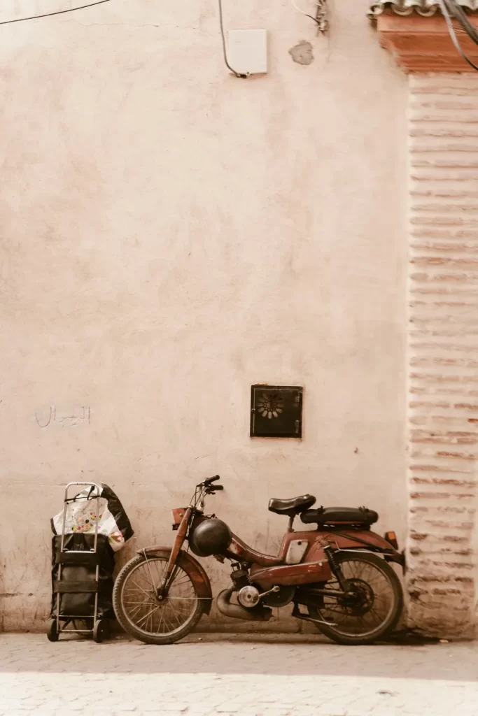 Ciclomotor antiguo y carro de la compra aparcados junto a una pared rosada de la medina