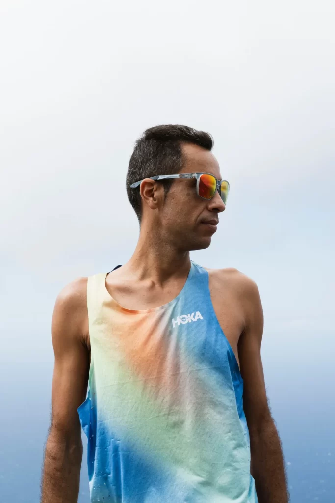 Corredor con camiseta Hoka y gafas de sol ante un cielo nublado