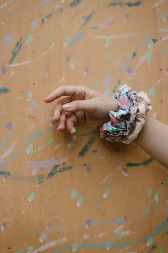 Mano con varios coleteros estampados en la muñeca ante una pared de madera salpicada de pintura