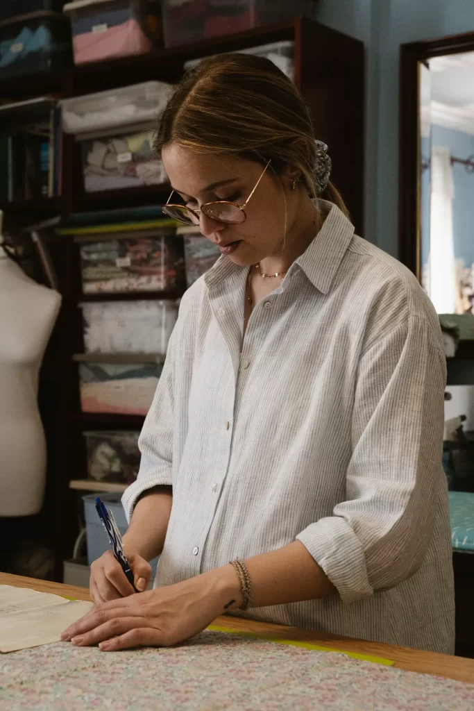 Mujer con gafas escribe sobre una mesa de costura en un taller con maniquí
