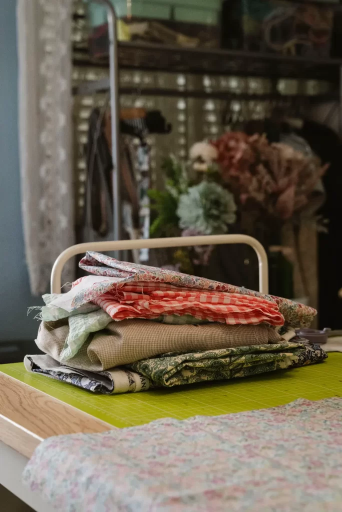 Pila de telas dobladas con estampados de flores, cuadros y cachemir sobre una base de corte verde