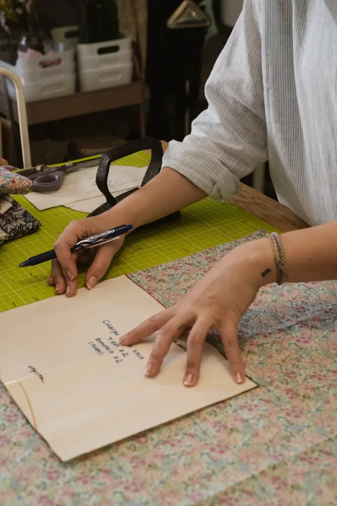 Manos colocando un patrón de papel sobre tela floral en una mesa de corte con tijeras y bolígrafo