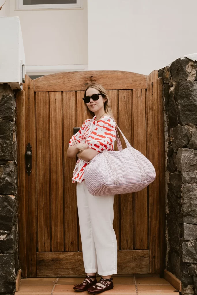 Mujer con gafas de sol y una bolsa acolchada de cuadros rosas al hombro ante una puerta de madera