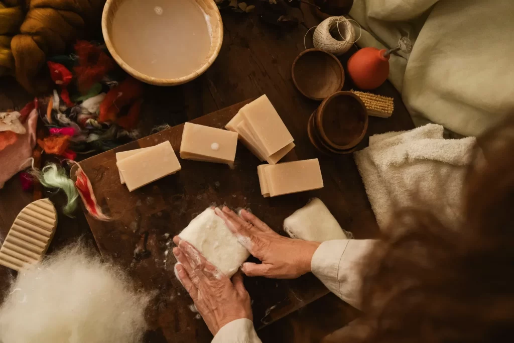 Vista cenital de manos enfieltrando una pastilla de jabón con lana y espuma sobre una tabla de madera