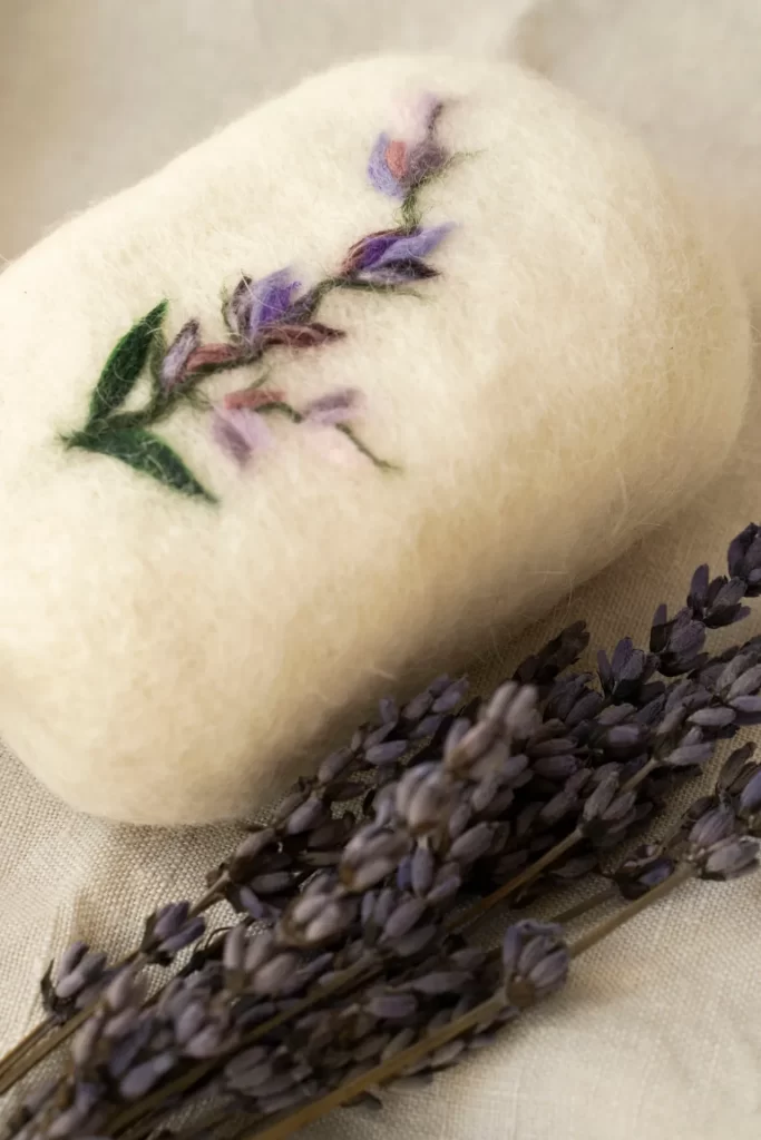 Jabón de fieltro blanco con una rama de flores lilas bordada junto a espigas de lavanda seca
