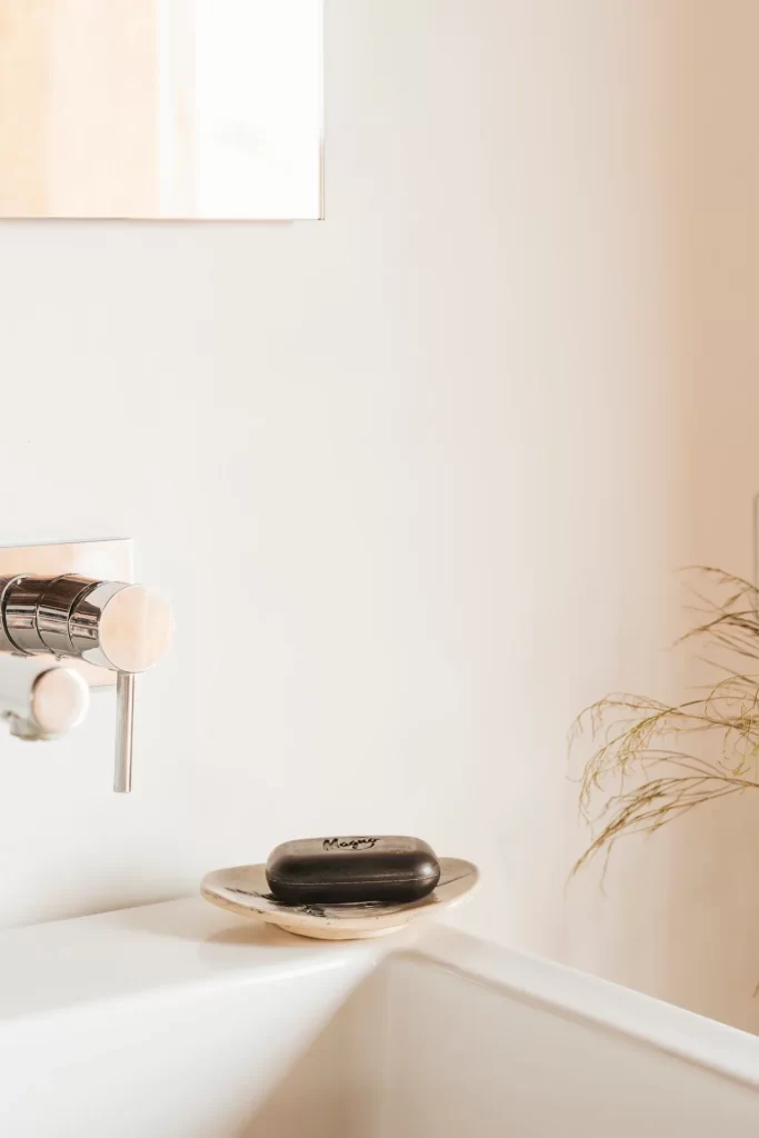 Pastilla de jabón negro en una jabonera de cerámica junto al grifo cromado de un lavabo blanco