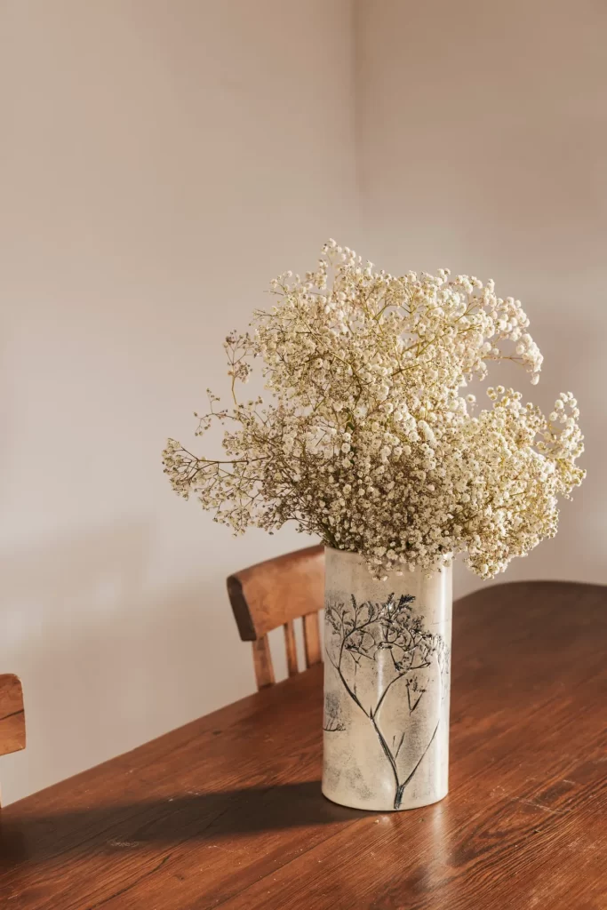 Jarrón de cerámica con relieve vegetal y ramo de paniculata sobre una mesa de madera