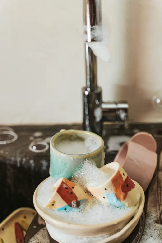 Tazas y cuencos de cerámica pintada cubiertos de espuma junto a un grifo