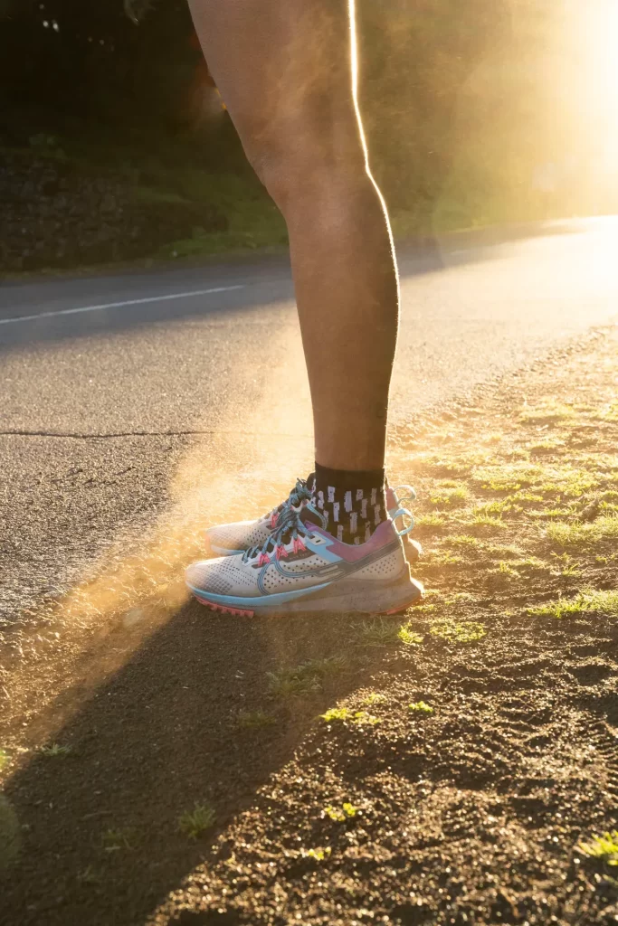 Pierna de corredora con zapatilla de trail levantando polvo al borde de una carretera a contraluz