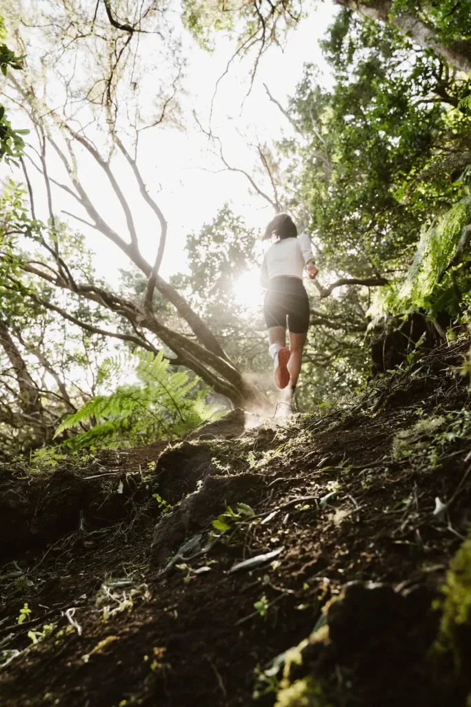 Corredora subiendo un sendero de tierra en un bosque de laurisilva con el sol filtrándose entre los árboles
