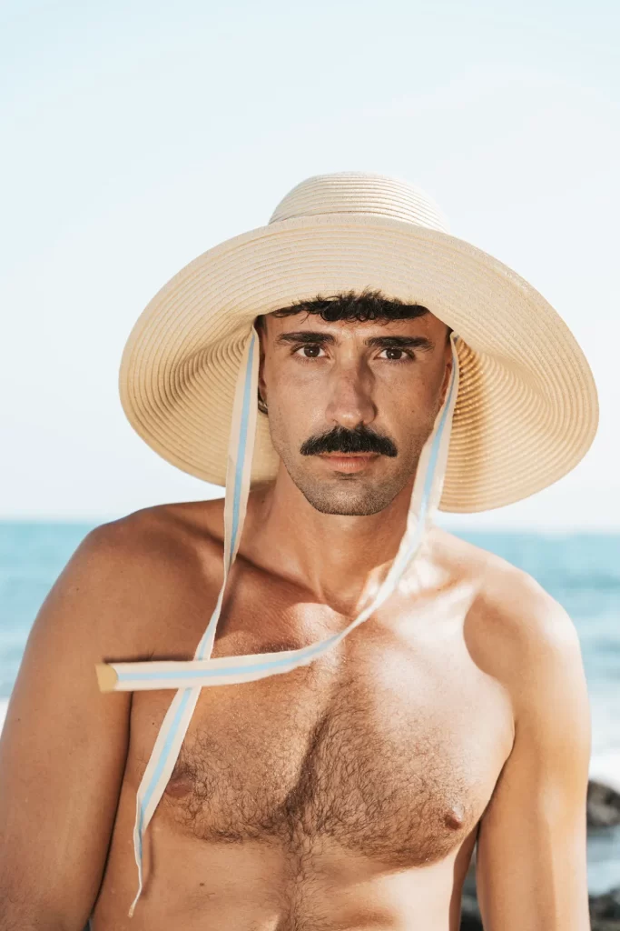 Retrato de hombre con bigote y sombrero de paja de ala ancha con cintas frente al mar