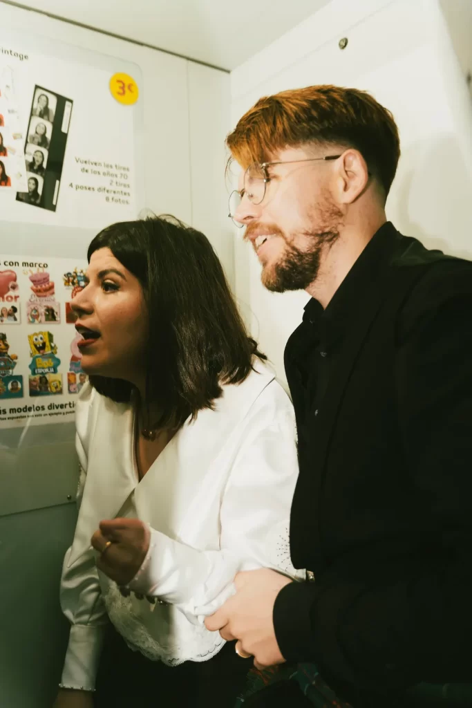 Pareja recién casada mirando sorprendida la pantalla dentro de una cabina de fotomatón