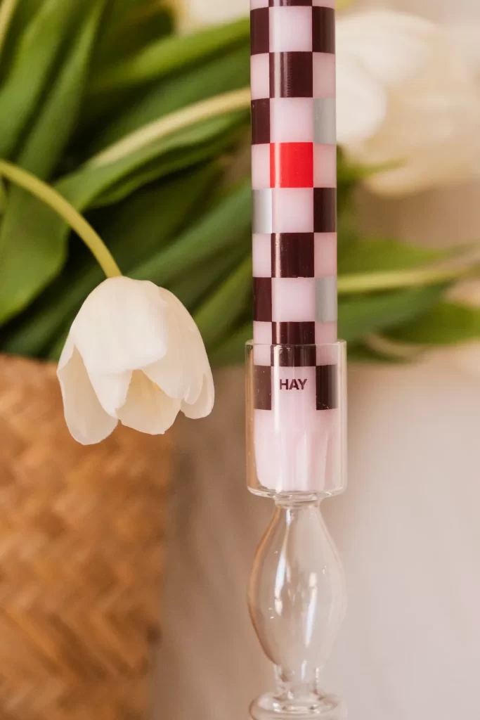 Vela de cuadros rosas y granates en un candelabro de cristal junto a un tulipán blanco