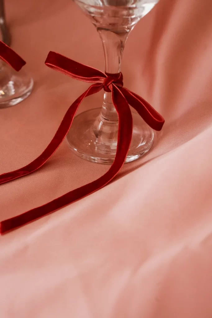 Lazo de terciopelo rojo atado al pie de una copa de cristal sobre una tela rosa