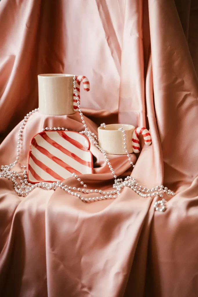 Tazas con asa de bastón de caramelo y plato a rayas rojas entre collares de perlas