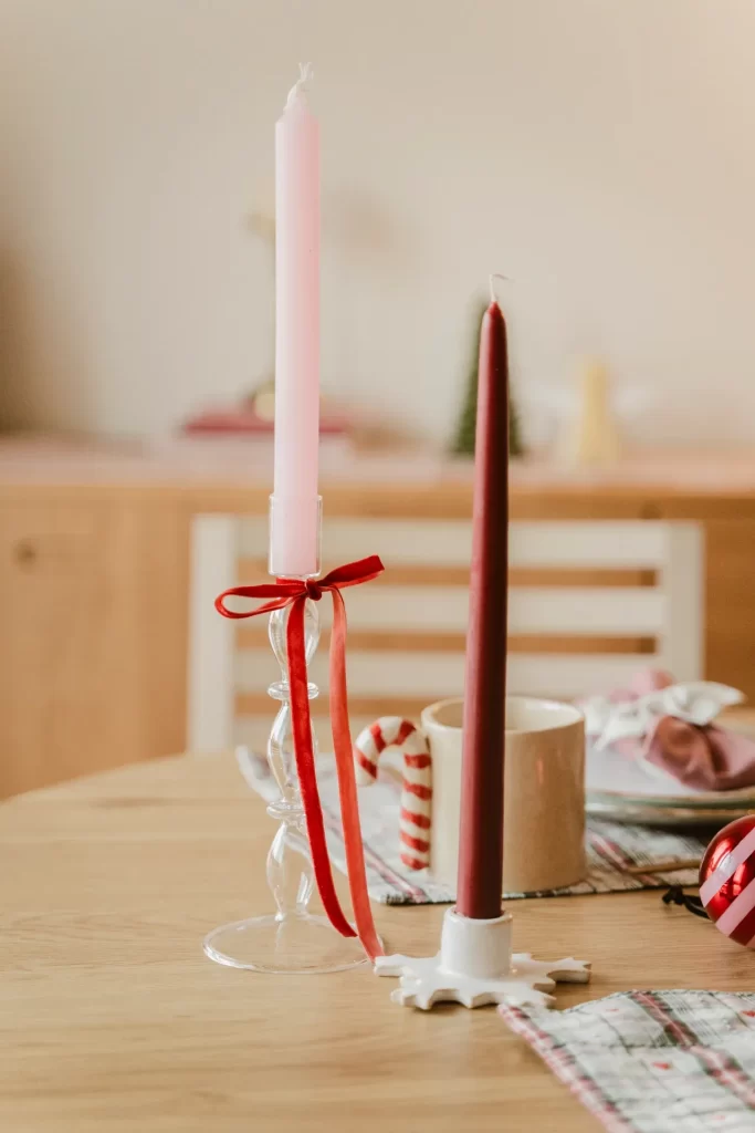 Vela rosa en candelabro de cristal con lazo rojo y vela granate sobre una mesa navideña de madera