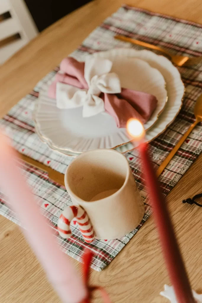 Plato blanco con servilleta rosa anudada, taza con asa de bastón de caramelo y mantel de cuadros