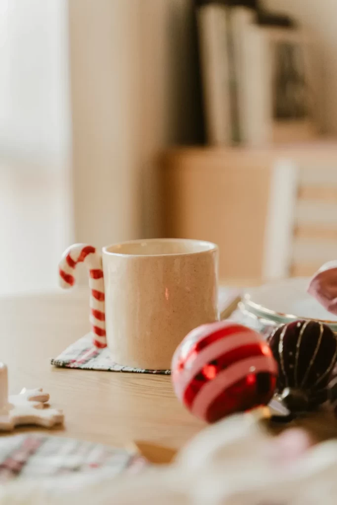 Taza de cerámica con asa de bastón de caramelo sobre una mesa con bolas navideñas