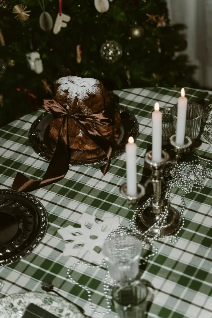 Bizcocho con azúcar glas y lazo marrón junto a un candelabro plateado sobre mantel verde de cuadros