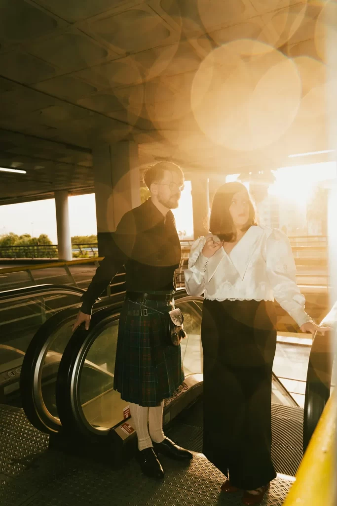 Pareja junto a unas escaleras mecánicas a contraluz, con destellos de sol