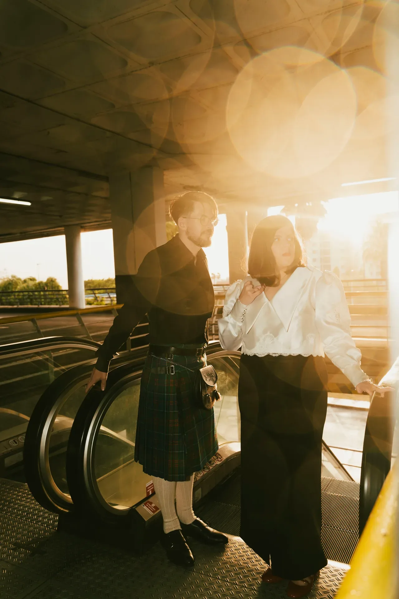 Pareja junto a unas escaleras mecánicas a contraluz, con destellos de sol