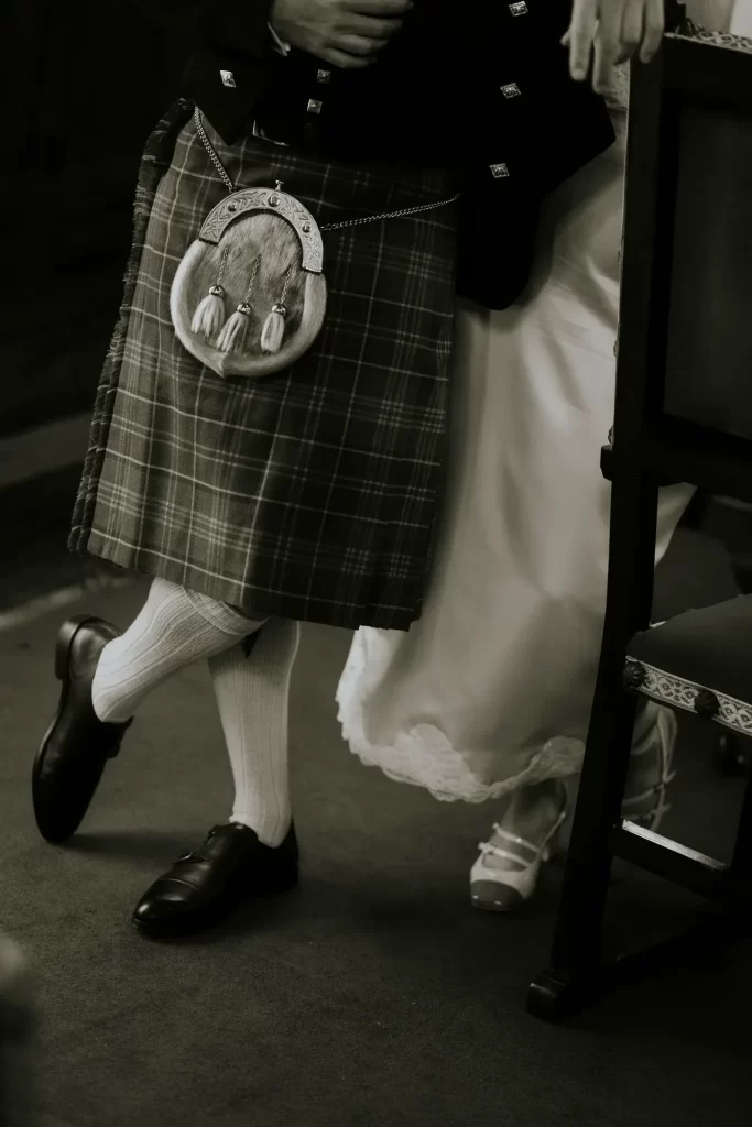 Detalle de las piernas del novio con kilt escocés y escarcela junto al vestido de la novia