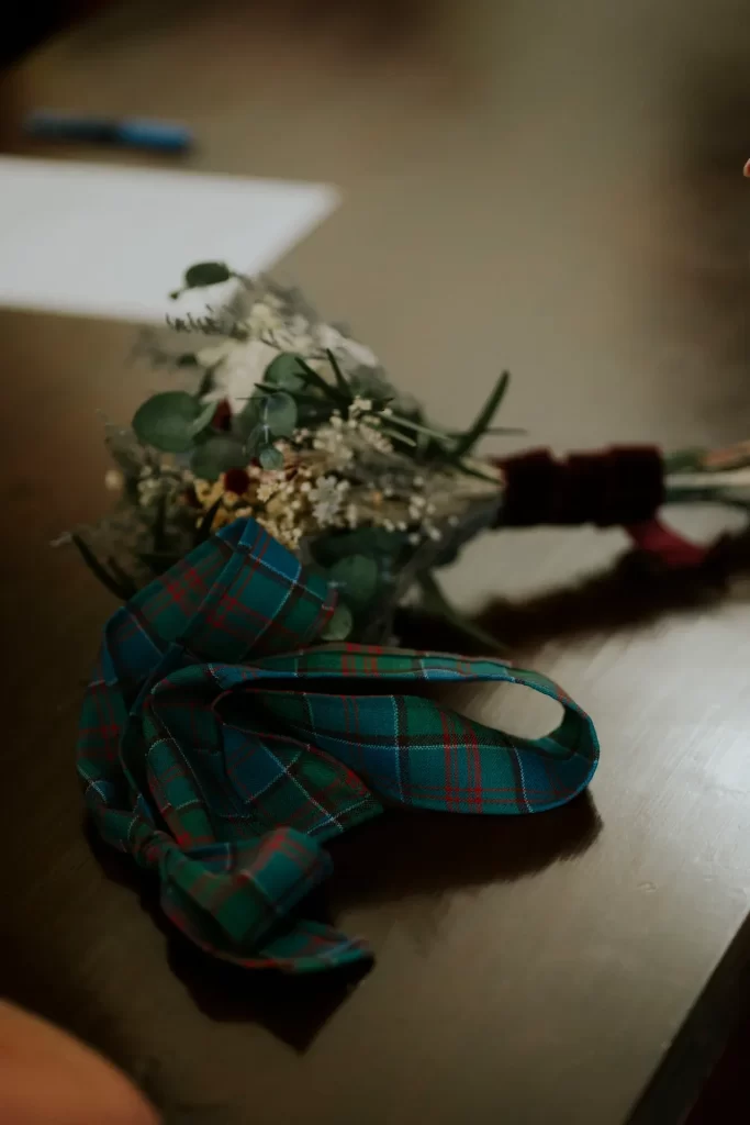 Cinta de tartán verde y azul junto a un ramo de flores secas sobre una mesa de madera