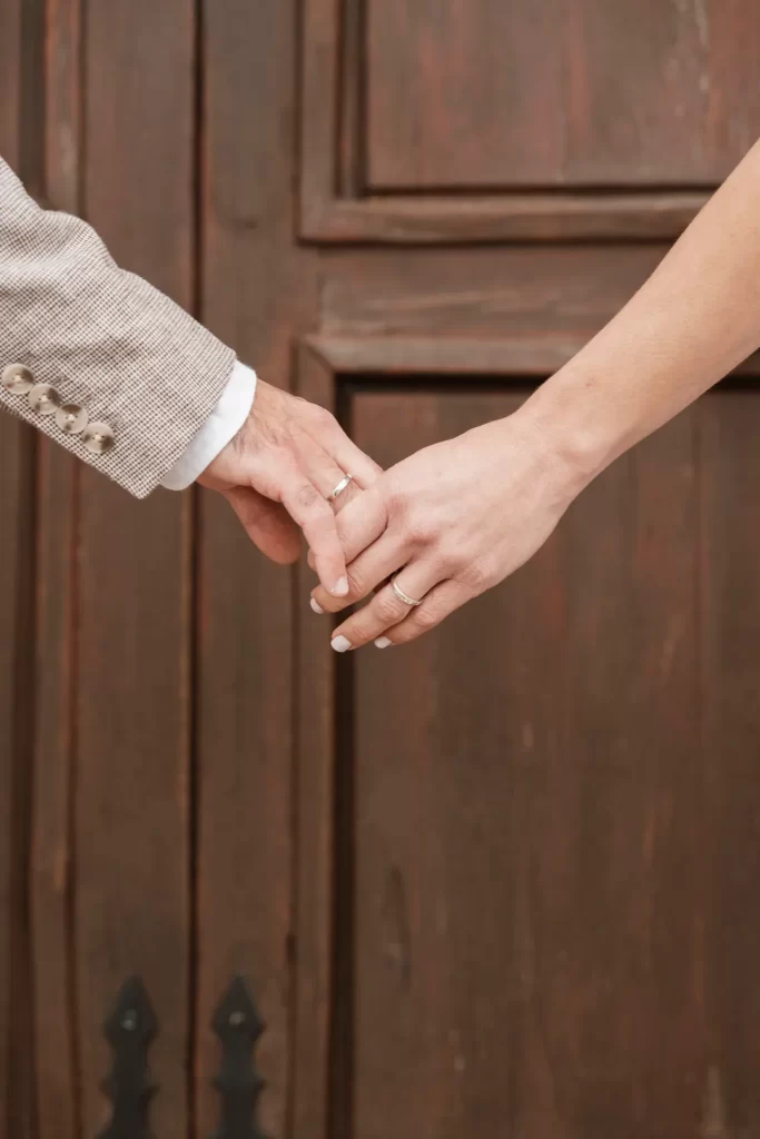 Manos de los novios cogidas con sus alianzas ante una puerta de madera oscura