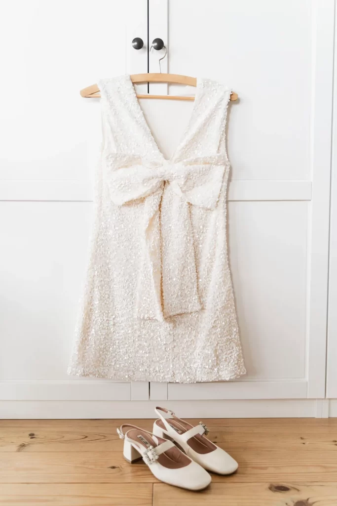 Vestido corto de lentejuelas con lazo colgado en una percha y zapatos blancos en el suelo