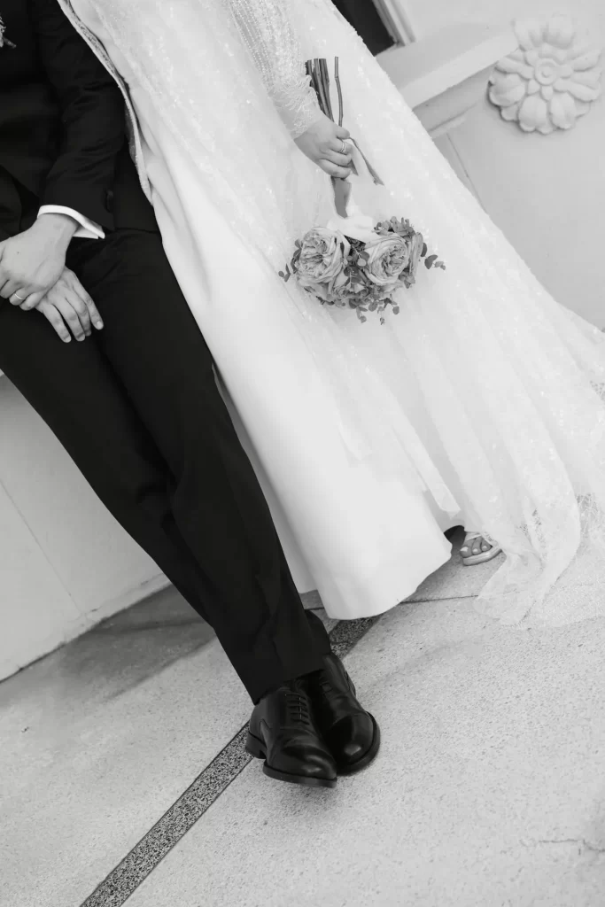 Detalle de las piernas de los novios con zapatos negros y el ramo de rosas sobre el vestido